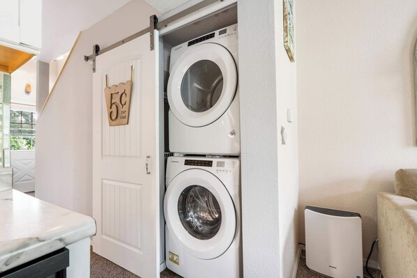 A laundry area with two stacked washing machines, a drying machine, and a door with a 5¢ per load sign.