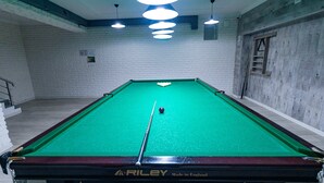 A pool table with a green felt surface, branded with "RILEY Made in England," in a room with white brick walls and a wooden floor.