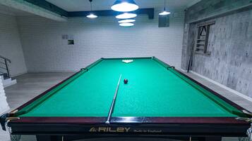 A pool table with a green felt surface, branded with "RILEY Made in England," in a room with white brick walls and a wooden floor.