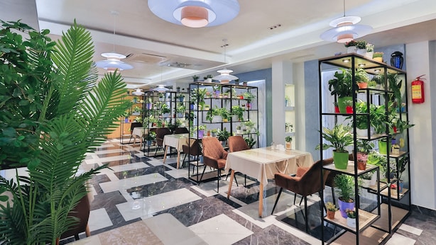 A modern indoor space with tables and chairs, surrounded by potted plants and shelves with more plants. - Safir Hotel  (Fergana)