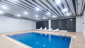 A swimming pool with clear blue water, surrounded by white lounge chairs and a tiled floor. - Safir Hotel  (Fergana)