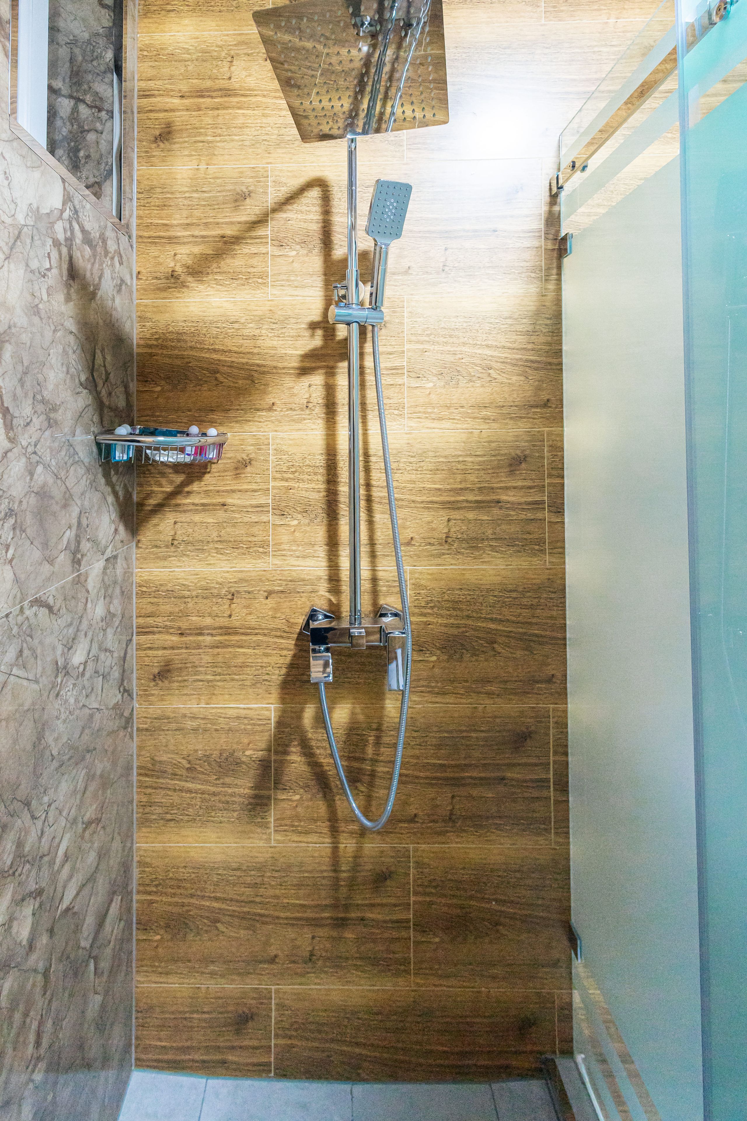 Une douche avec un mur en bois, un sol carrelé de marbre et une porte en verre.