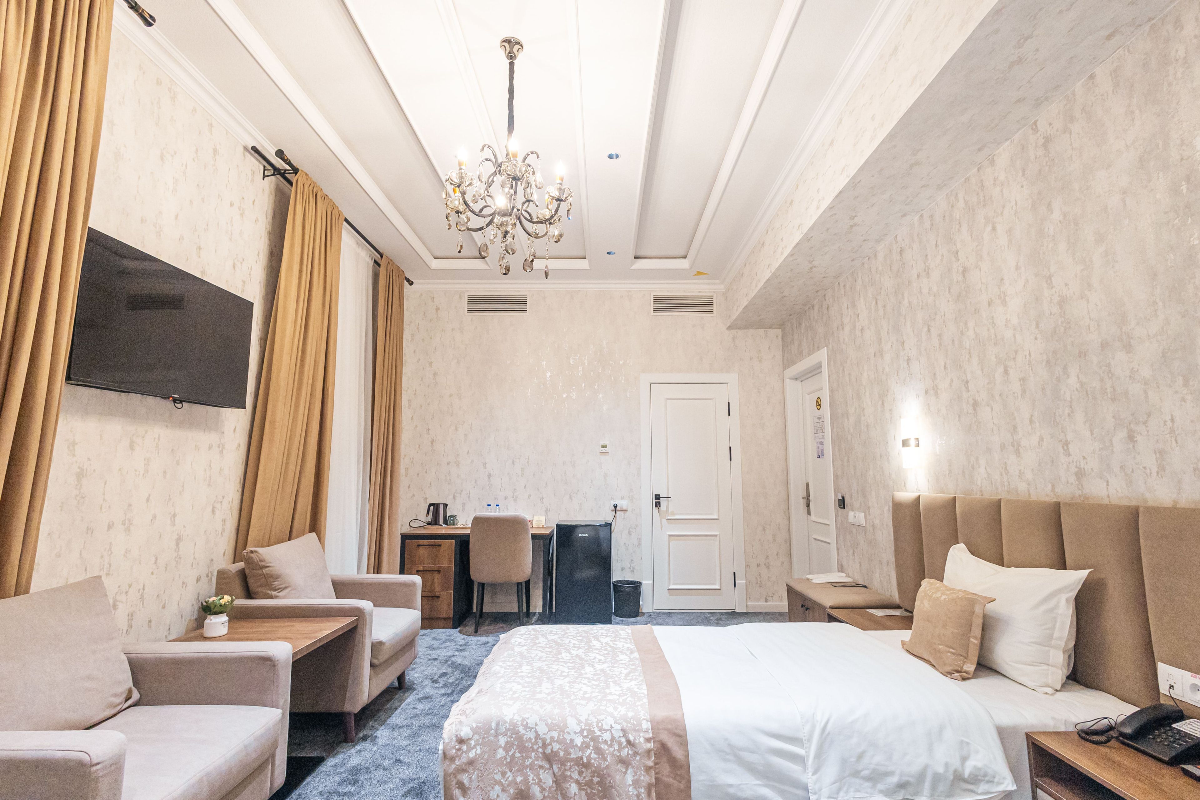 Une chambre d’hôtel équipée d’un lit, d’un bureau, d’une chaise, d’une télévision et d’un lustre.