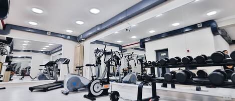 A gym with cardio machines, weight racks, and a mirrored wall.