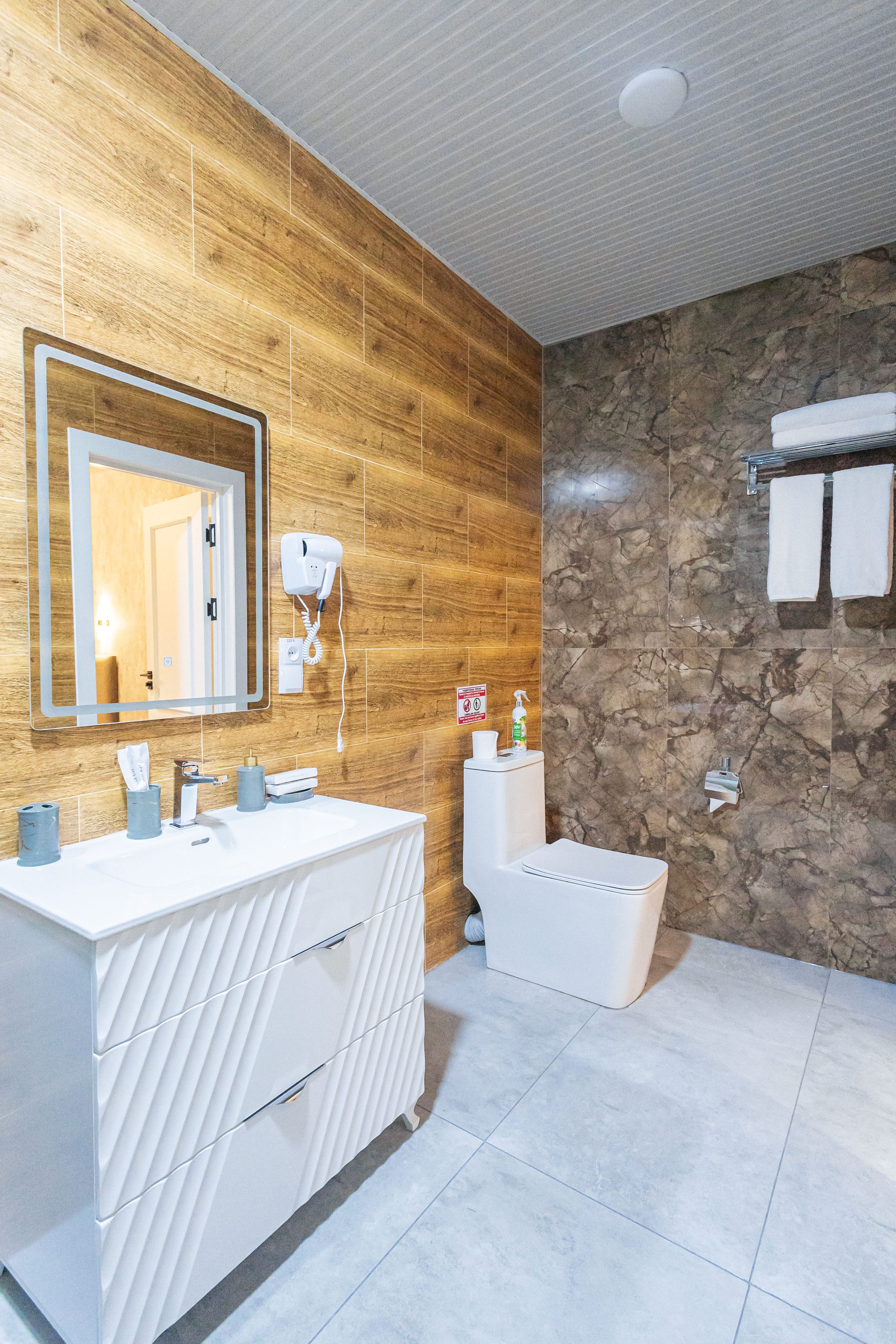Ein modernes Badezimmer mit Holzvertäfelung, einem großen Spiegel, einem weißen Waschtisch, einer Badewanne und einem Handtuchhalter.