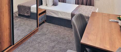 A modern hotel room with a bed, a desk, a chair, a mirror, and a television.