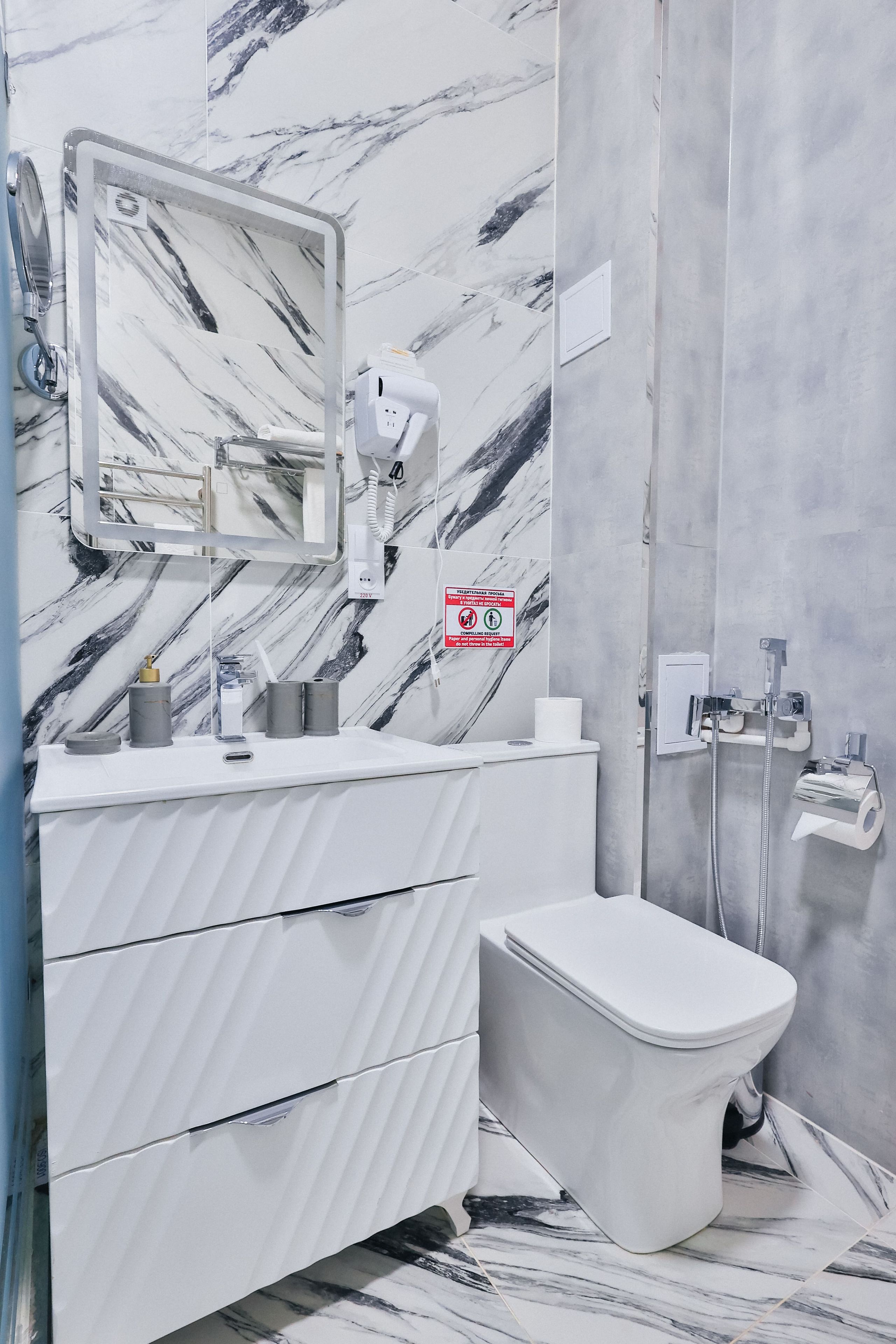 Ein Badezimmer mit Marmorfliesen, einem weißen Waschbecken, einer Toilette und einer Duschkabine.