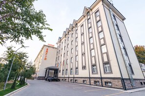 A multi-story hotel with a modern facade, a covered entrance, and a parking area. - Safir Hotel  (Fergana)