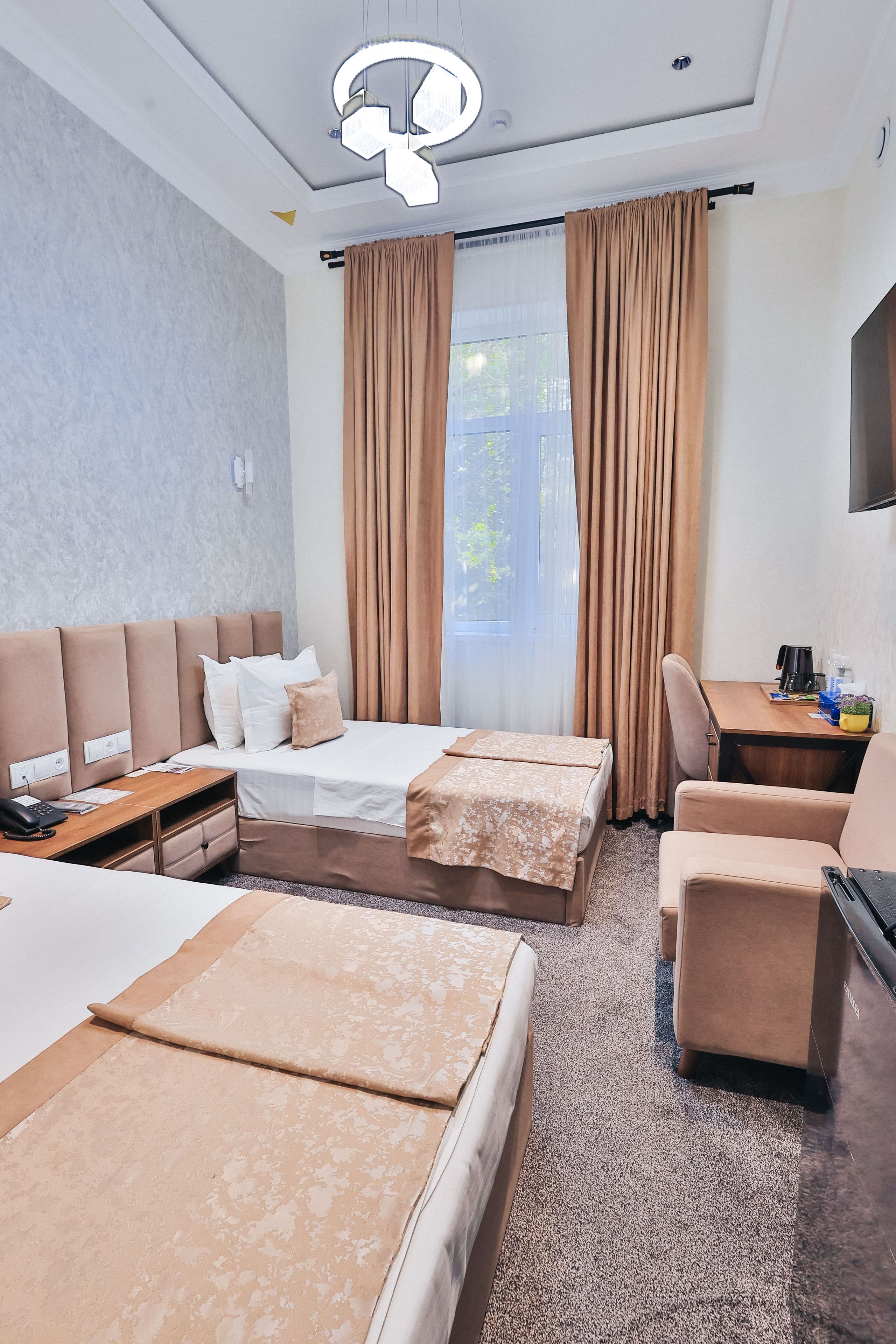 A hotel room with two beds, a desk, a chair, a TV, and a large window with curtains.