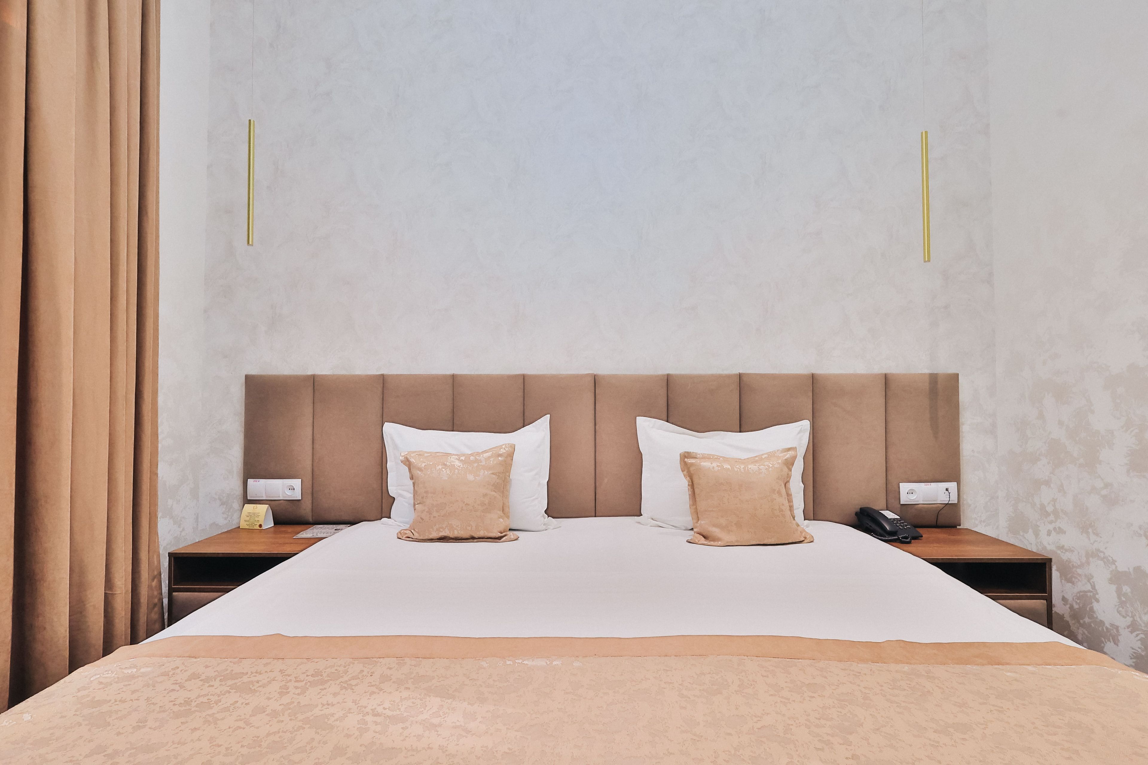 A hotel room with a large bed, two bedside tables, a headboard, and a curtain.