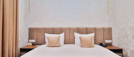 Una habitación de hotel con una cama grande, dos mesitas de noche, un cabecero y una cortina.