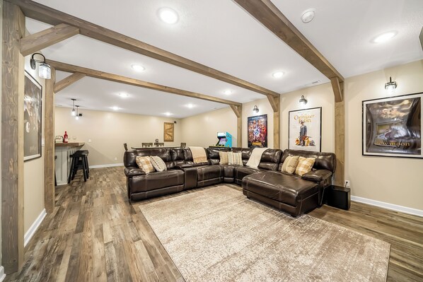 Un salón espacioso con un sofá modular, vigas de madera y un tapete grande.