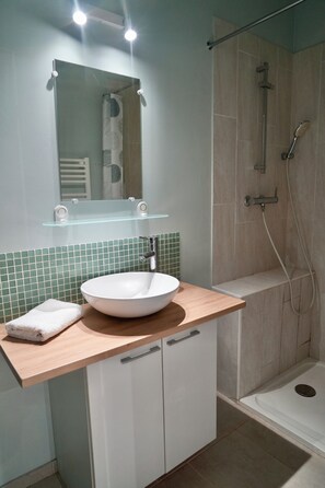 Un baño con un lavabo blanco, un estante de vidrio arriba y una zona de ducha.