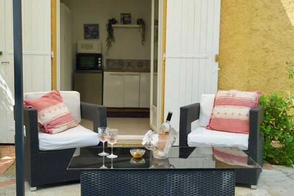 Un conjunto de sofá de mimbre con cojines blancos y una mesa de vidrio con una botella y vasos.