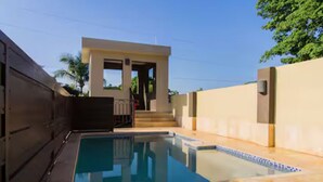 A swimming pool with a clear blue water surface, surrounded by a beige wall and a dark fence. - Star Tree- 2 Bedroom Condo 10 mins to New Kingston (Kingston)