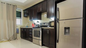 A modern kitchen with dark wooden cabinets, stainless steel appliances, and a water dispenser. - Star Tree- 2 Bedroom Condo 10 mins to New Kingston (Kingston)