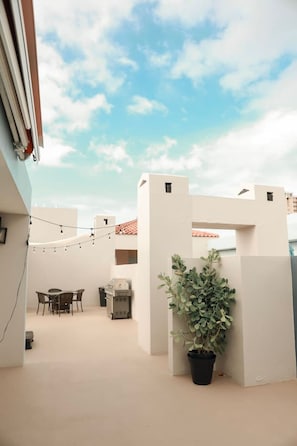 A rooftop terrace with a dining area, a potted plant, and a string of lights.