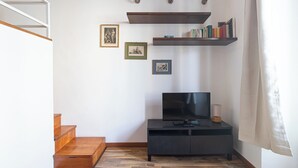 Quarto com televisão em suporte preto, escadas de madeira e quadros na parede.