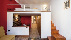 Quarto compacto com beliche, pequena escrivaninha e uma cadeira. Escada leva a outro andar.