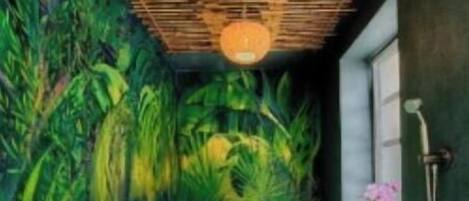 A bathroom with a large bathtub, a wooden ceiling, and a mural of tropical foliage.