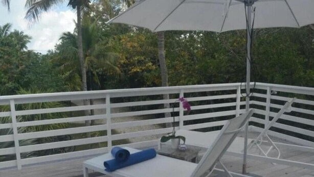 Eine Terrasse mit weißer Geländer, ein Liegestuhl, ein blaues Handtuch und ein großer Sonnenschirm.