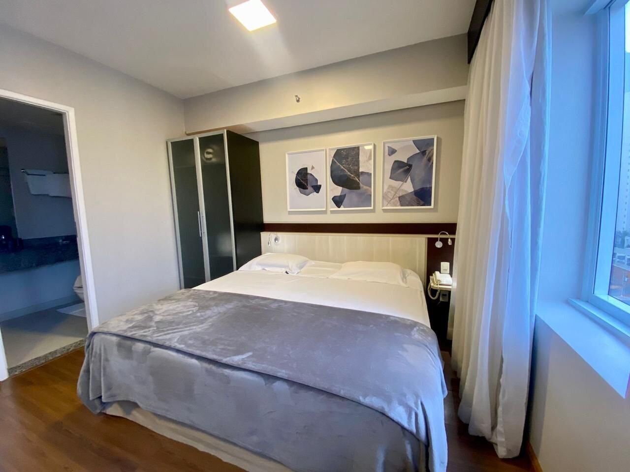 A modern hotel room with a large bed, a wardrobe, and a window with curtains.
