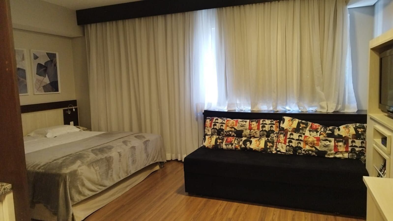 Una habitación de hotel con cama, sofá, mesita de noche y ventana con cortinas.