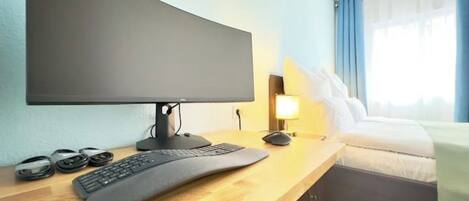 Une chambre d’hôtel équipée d’un bureau, d’un grand téléviseur à écran plat, d’un clavier et d’une souris.