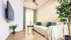 A modern living room with a sofa, a small table, a ceiling fan, a TV mounted on the wall, and a potted plant. - Playa del Cura, 3 min to the beach, Central, Free parking (Torrevieja)