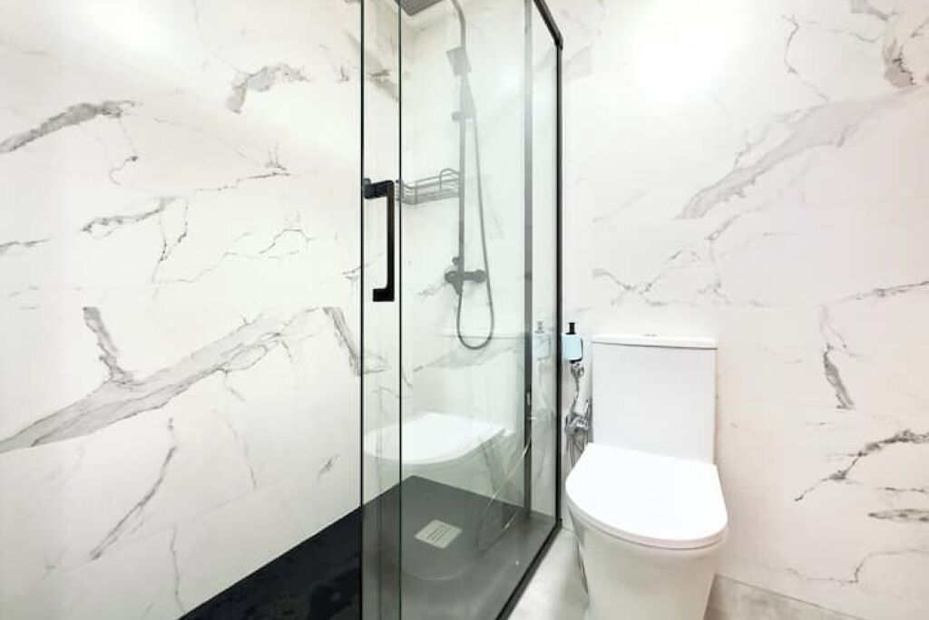 Et moderne badeværelse med en glasafskærmet brusekabine, et hvidt toilet og vægge med marmorering.