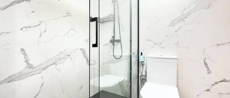 Et moderne badeværelse med en glasafskærmet brusekabine, et hvidt toilet og vægge med marmorering.