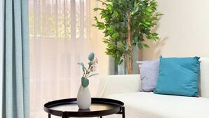 A room with a white sofa, a blue cushion, a small round table with a white vase, and a large green plant. - Playa del Cura, 3 min to the beach, Central, Free parking (Torrevieja)