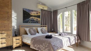 Ein Schlafzimmer mit einem großen Bett, Nachttischen aus Holz, einem Gemälde und einem Fenster mit Vorhängen.