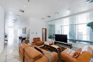 Ein geräumiges Wohnzimmer mit großem Flachbildfernseher, Ledersofas und einem Glastisch.