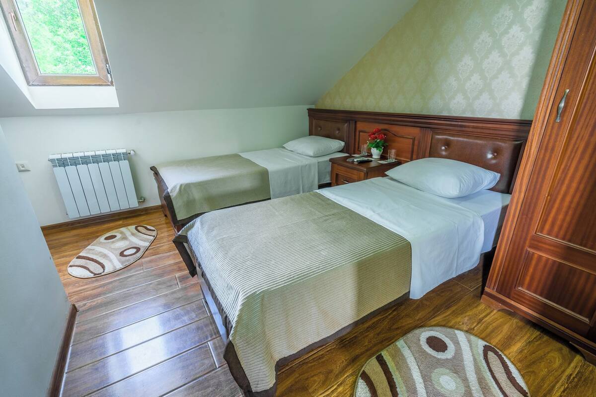 A bedroom with two beds, a radiator, wooden flooring, and a window.