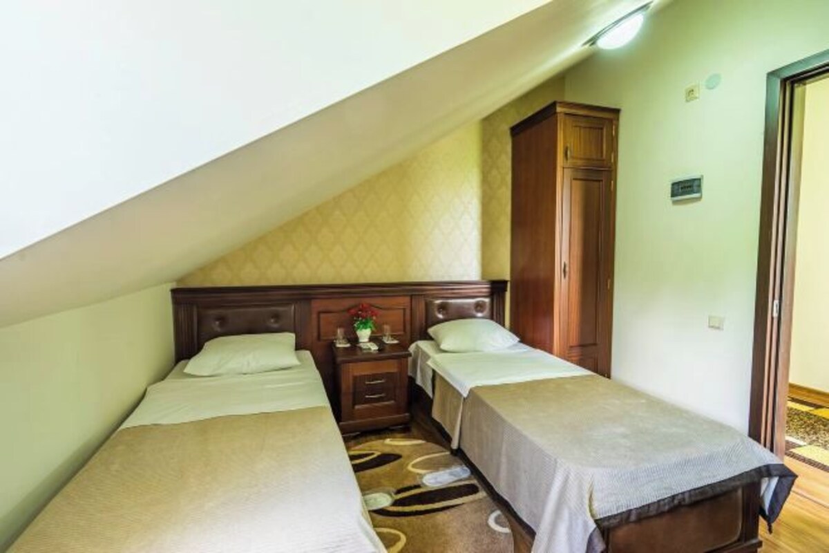 Una stanza con due letti singoli, un'armadio in legno, un comodino con una lampada e un tavolino con un vaso.