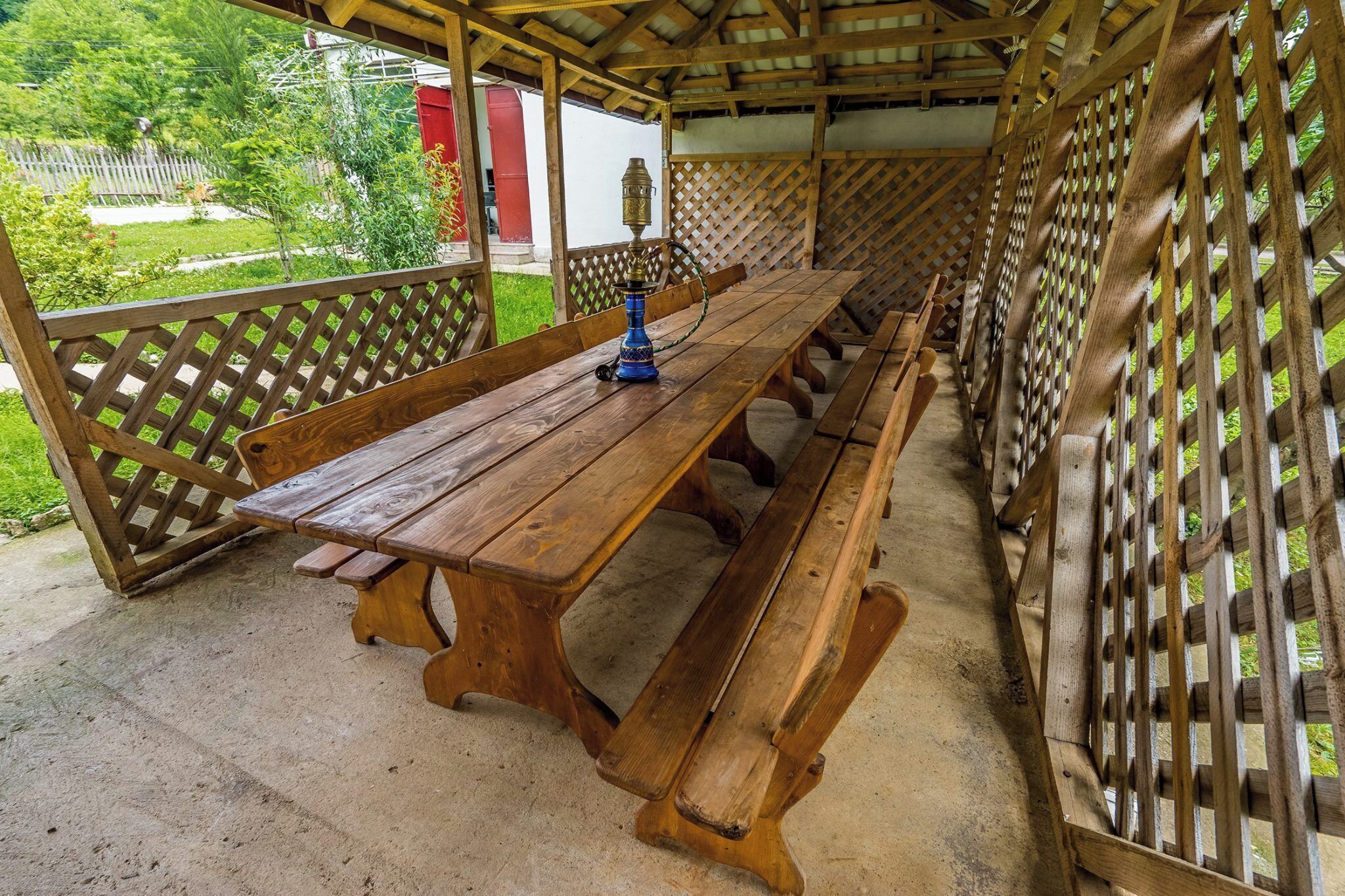 Una mesa de picnic de madera con bancos bajo una pérgola de madera con celosías.