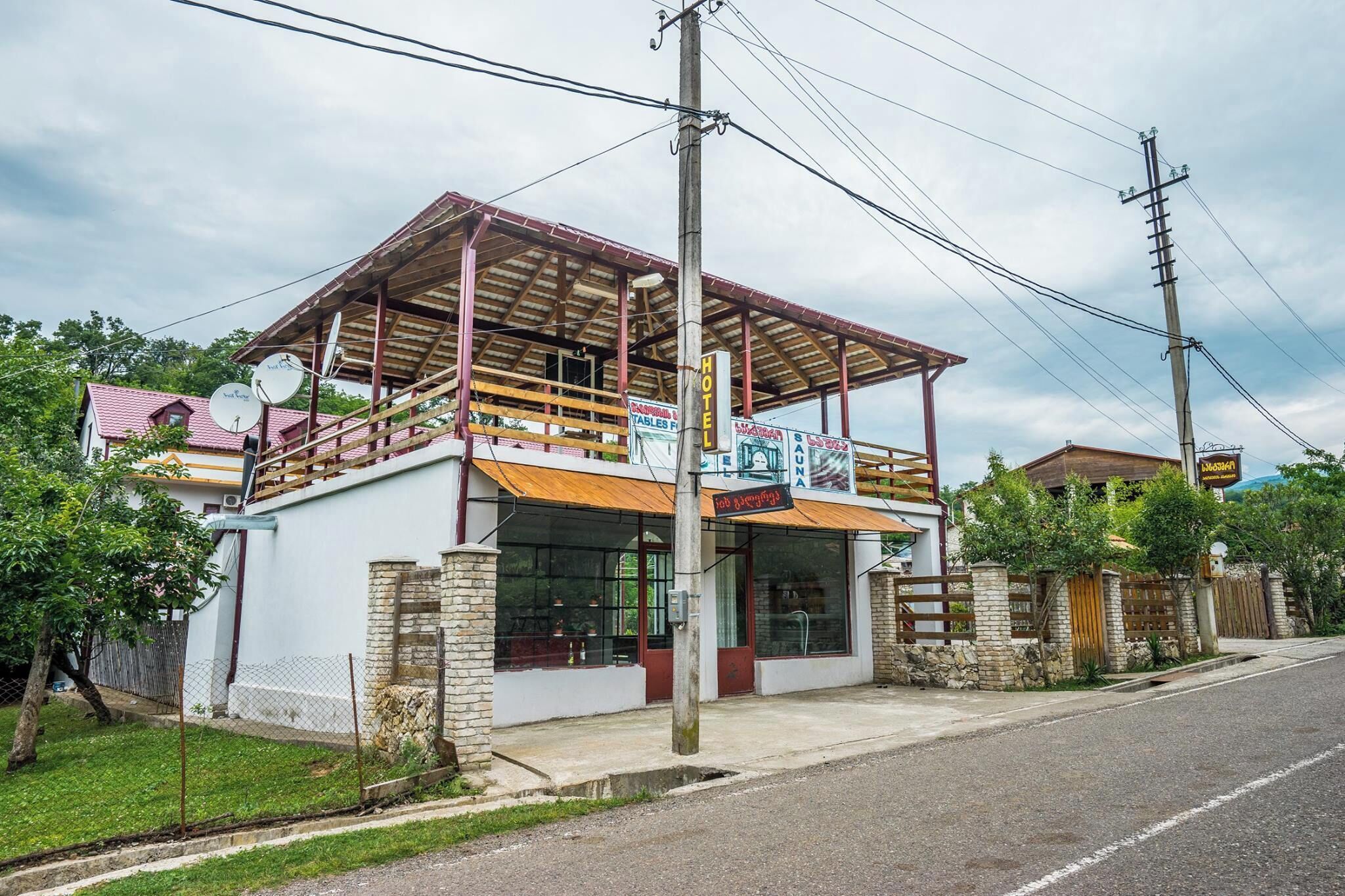 A two-story building with a sign indicating it is a hotel. There are satellite dishes on the roof, and the building has a wooden balcony.
