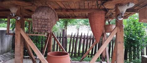 A rustic wooden structure with a thatched roof, a large terracotta pot, and woven baskets hanging from the beams.