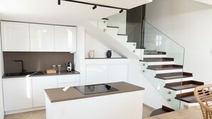 Een moderne keuken met witte kasten, een centraal eiland en een glazen trap.