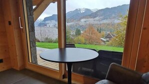 A room with a table and a chair, a sliding glass door leading to a mountain view. - Chalet neuf standing Samoëns - Adults only (15+) (Samoëns)