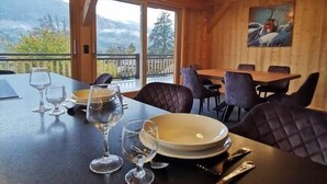 A wooden dining area with a table set for two, large windows, and a painting on the wall. - Chalet neuf standing Samoëns - Adults only (15+) (Samoëns)