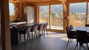 A modern kitchen with a bar area, large windows, and a dining space with chairs. - Chalet neuf standing Samoëns - Adults only (15+) (Samoëns)