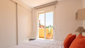 Un dormitorio con cama, una silla, una lámpara y vistas al exterior.