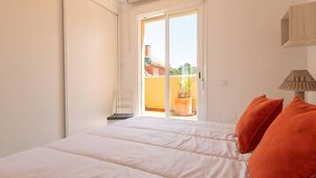 Ein Schlafzimmer mit Bett, Stuhl, Lampe und Blick ins Freie.