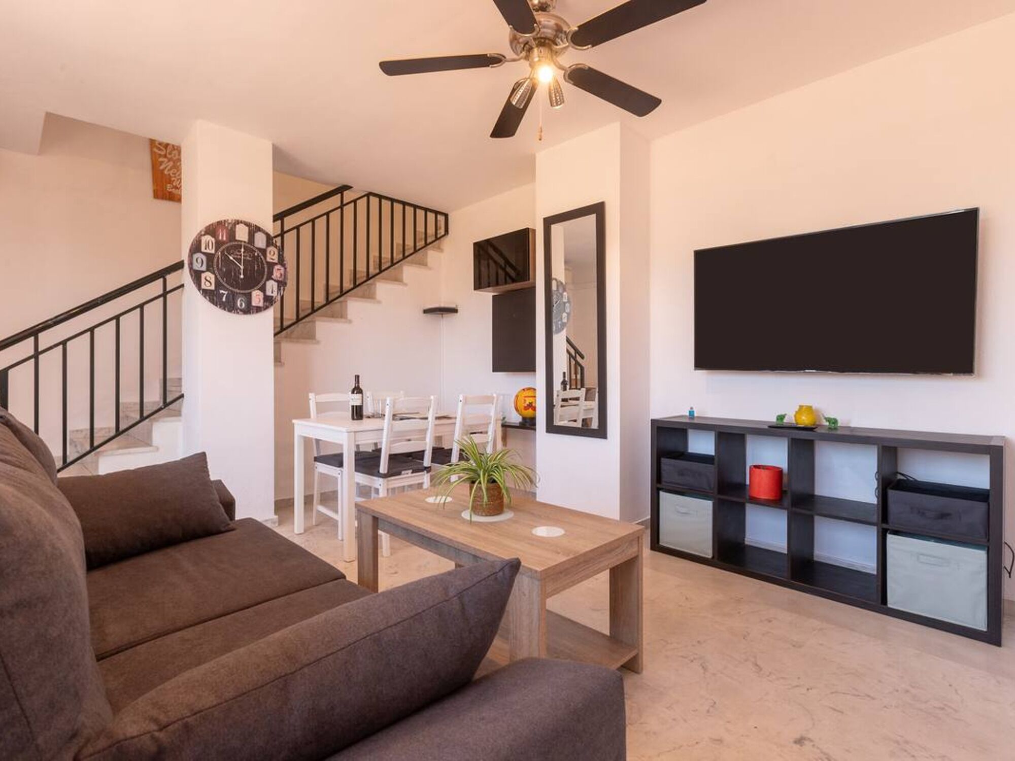 Ein modernes Wohnzimmer mit Sofa, Couchtisch, Fernseher, einer Treppe und einem Essbereich.