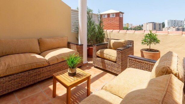 Una terraza en la azotea con mobiliario de mimbre, una mesita y plantas en macetas.