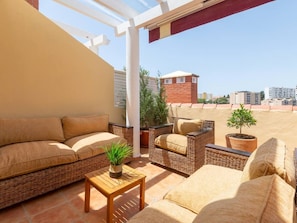 Une terrasse sur le toit, aménagée avec des meubles en osier, une petite table et des plantes en pot.