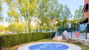 Una piscina rodeada por un muro de piedra, con un césped y árboles al fondo.