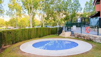 Una piscina rodeada por un muro de piedra, con un césped y árboles al fondo.